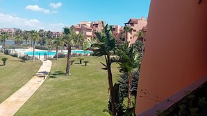 Une vue d’un complexe hôtelier avec une piscine, des palmiers et un ciel bleu azur.
