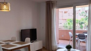 Un salon équipé d’un téléviseur, d’une table à manger et d’un balcon avec du mobilier d’extérieur.