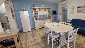 A compact living space with a dining table, chairs, a blue sofa, a white cabinet, and a tiled floor. - ON THE SEA Casalbordino Lido Costa dei Trabocchi (Termini)