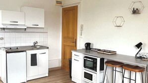 Una cocina compacta con armarios blancos, horno empotrado, máquina de café y un taburete de bar.