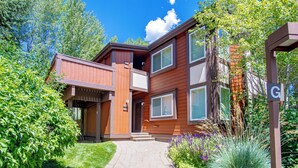 A two-story building with a balcony, a brick pathway, and a garden with various plants. - Atelier Lookout - 2BD Condo Baldy Views + Pool (Sun Valley)