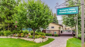 A pathway leading to a building labeled "Olympic Pool Tennis Center," surrounded by lush greenery and a well-maintained lawn. - Atelier Lookout - 2BD Condo Baldy Views + Pool (Sun Valley)