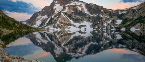 A mountain reflected in a calm lake with rocky terrain and sparse vegetation.