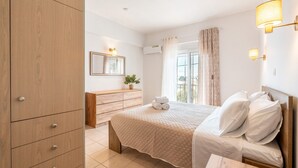 Habitación de hotel con cama, armario de madera, mesita de noche, espejo y ventana con cortinas.