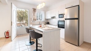 Una cocina moderna con una isla central, taburetes de bar, electrodomésticos de acero inoxidable y vistas a través de una puerta abierta.