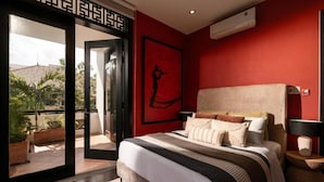A bedroom with a large bed, a red wall, and a view of the outdoors.