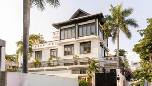 A two-story house with a balcony, a gated entrance, and palm trees.
