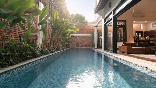 A swimming pool with a tiled edge, surrounded by greenery and a brick wall.
