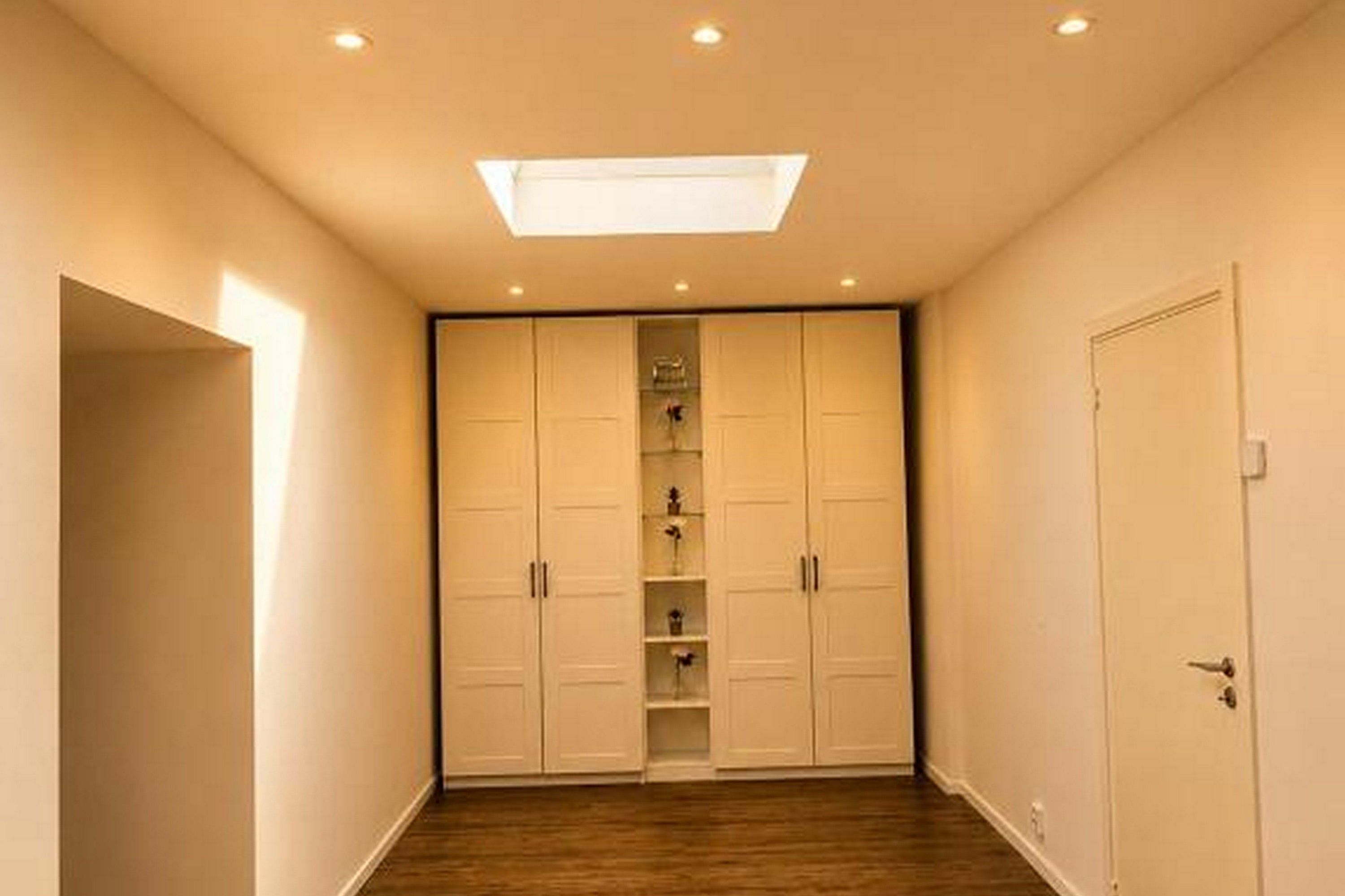 A hallway with a ceiling light, a wardrobe with multiple doors, and a door on the right.