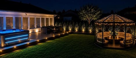 A well-lit outdoor area with a hot tub, a covered seating area, and a gazebo.