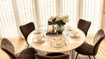 A round dining table set for six with a vase of white flowers, a sign reading 'Dine Couture,' and a book titled 'Dine Couture.'