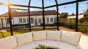 Un espacio de estar al aire libre cubierto, con vistas a una casa y jardín.