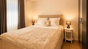 A hotel room with a large bed, two bedside tables with lamps, a headboard, and a window with curtains. - Seavista Trelleborg Sea View & Jacuzzi (Trelleborg)