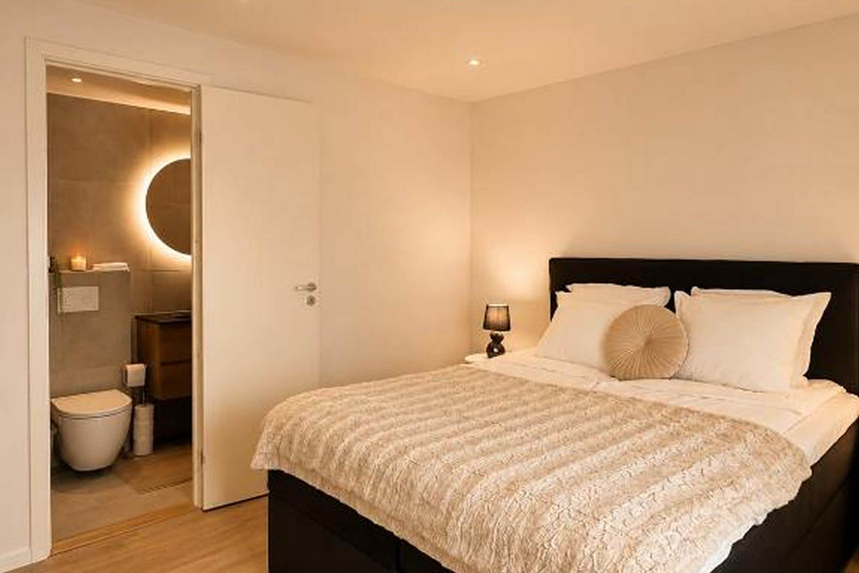 A bedroom with a bed, a bedside table with a lamp, and a circular wall light.