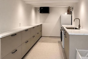 Una cocina moderna con lavadora integrada, un lavamanos y un televisor de pantalla plana montado sobre la encimera.