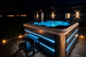 A hot tub with LED lighting, a wooden deck, and a modern building in the background.