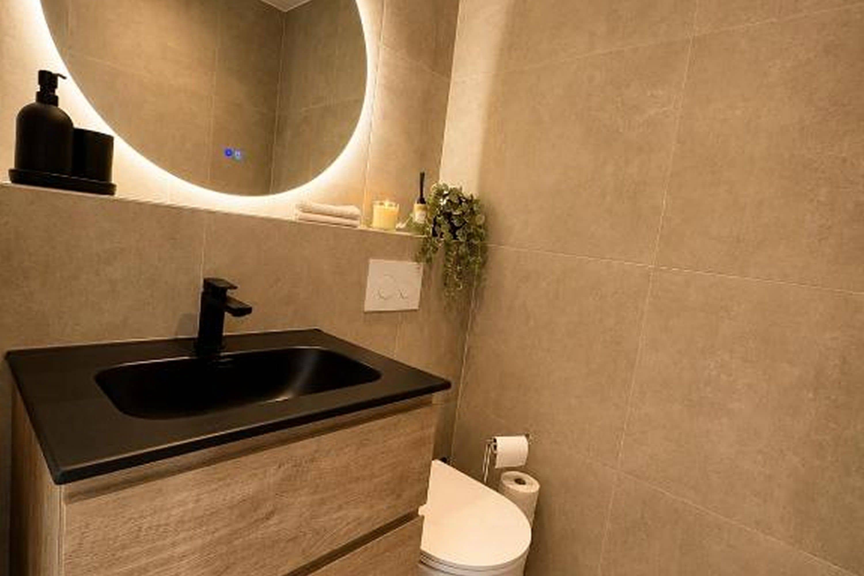 A bathroom with a black sink, a toilet, and a mirror.