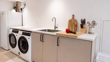 Een kleine keuken met een wasmachine, een spoelbak en een snijplank met groenten.