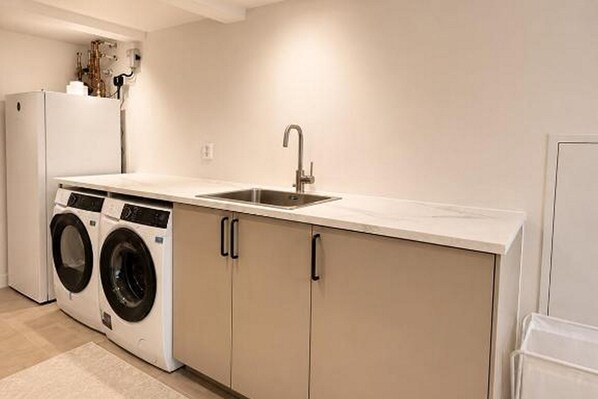 A compact kitchen with a sink, two washing machines, and a refrigerator.