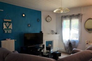 Un salon comprenant un téléviseur, un canapé, une table basse en verre, des éléments décoratifs muraux, une horloge et une fenêtre avec des rideaux.
