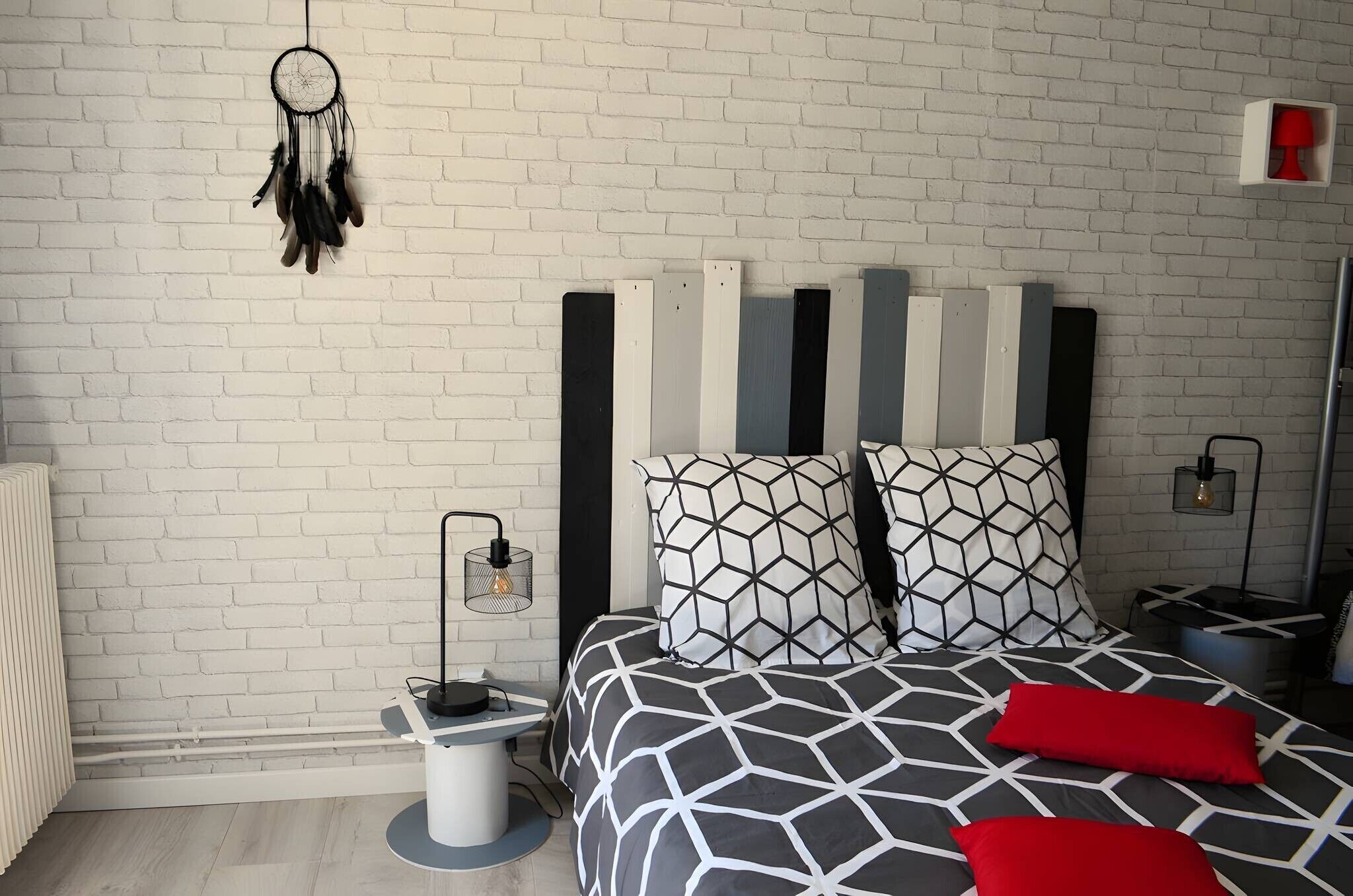A modern bedroom with a white brick wall, a geometric patterned bedspread, and a dreamcatcher.