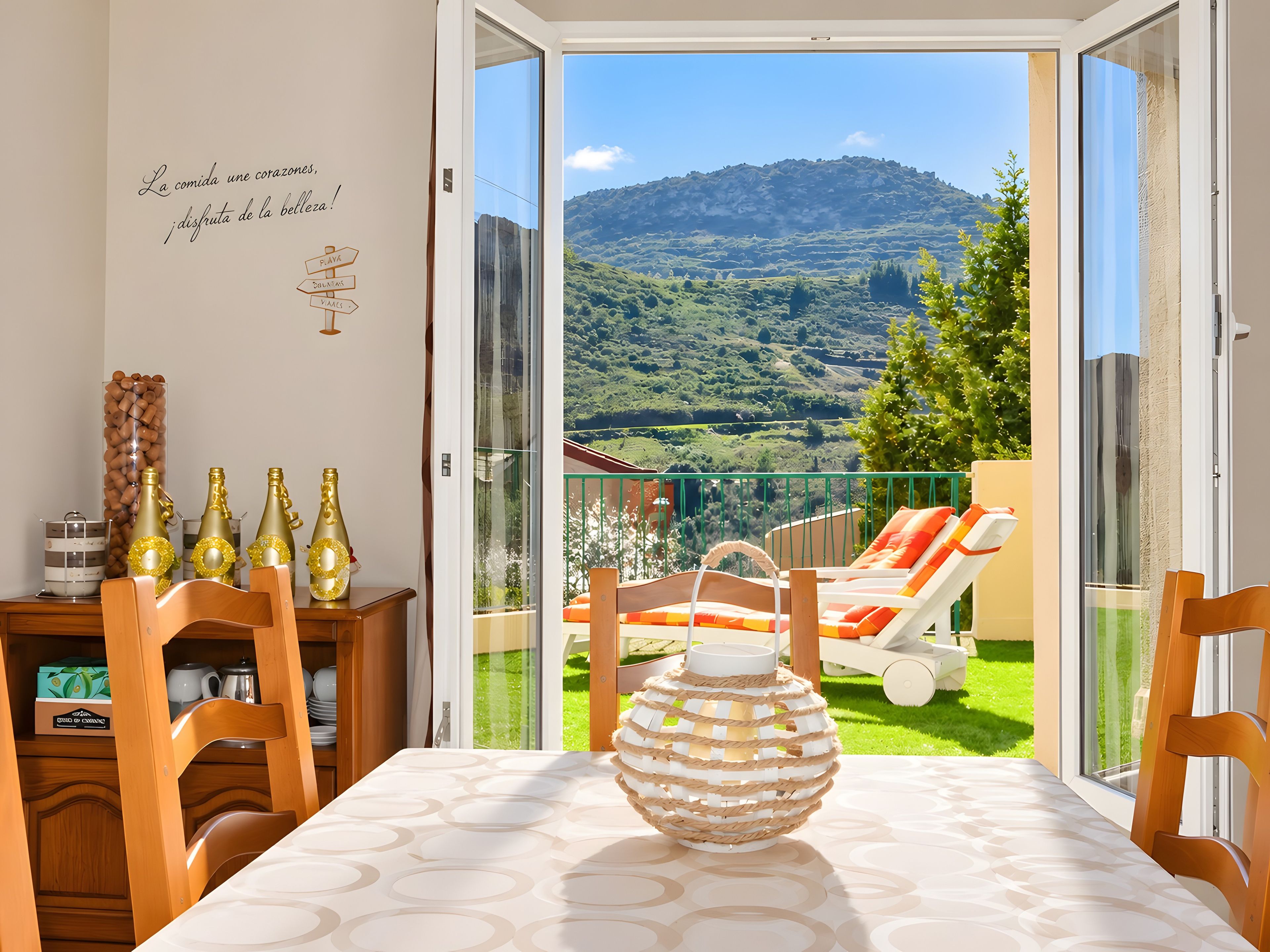 Un balcon donnant sur un paysage verdoyant et des montagnes, une table avec un vase, et un mur orné d’une inscription.