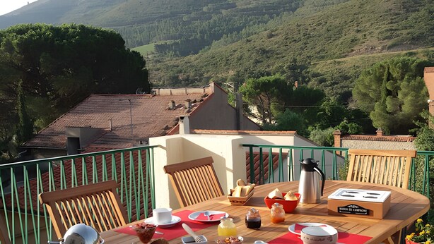 Une table en bois, dressée pour le petit-déjeuner, avec une vue sur les montagnes et une rambarde verte.