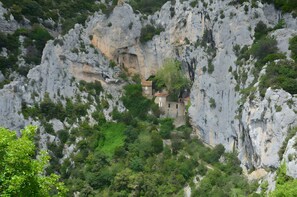 Un edifici petit arrecerat en un penya-segat rocos amb vegetació densa al voltant.