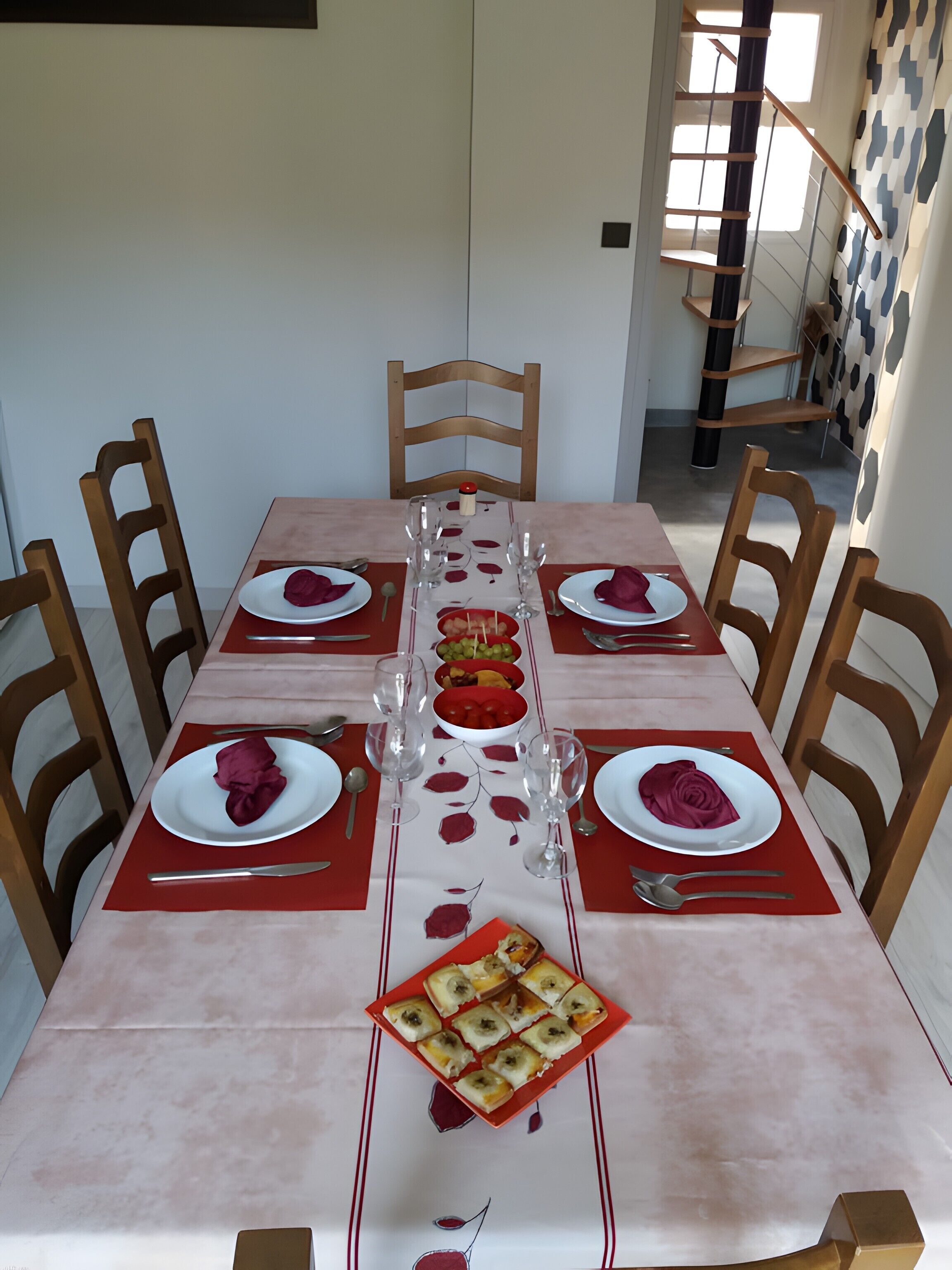 A dining table set with plates, glasses, and cutlery, surrounded by wooden chairs.