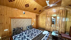 A wooden cabin room with a bed, a chair, a small table, and a ceiling fan. - Behtereen Resort (Srinagar)
