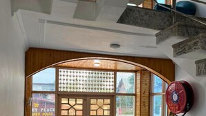 A room with a blue sofa, a wooden-framed window, and a red fan. - Behtereen Resort (Srinagar)