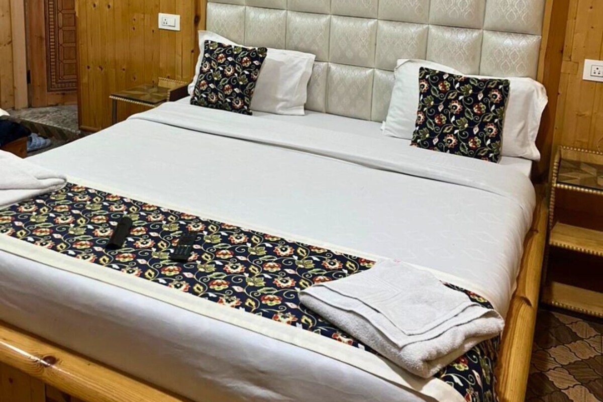 Una habitación con paneles de madera, una cama con cabecera tapizada, ropa de cama blanca y almohadas estampadas.