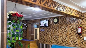 A reception area with a blue sofa, wooden panel wall, reception desk, hanging plants, and a clock. - Behtereen Resort (Srinagar)