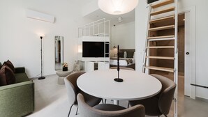 Uma sala de estar moderna com uma mesa redonda, cadeiras, uma televisão e um ventilador de teto branco.