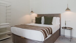 Cama bem arrumada com manta listrada, mesa de cabeceira com abajur e prateleira na parede.