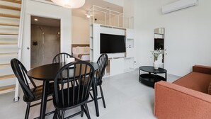 A modern living room with a dining area, a sofa, a TV mounted on the wall, and a staircase leading to an upper level. - Comfort and Design Facing the Turia Gardens in Valencia (Valencia)
