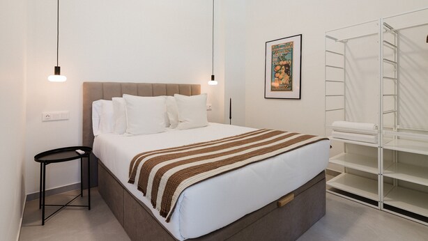 A neatly arranged hotel room with a bed, bedside table, and a built-in wardrobe. - Comfort and Design Facing the Turia Gardens in Valencia (Valencia)
