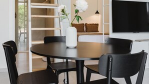 A modern dining area with a round table, black chairs, a white vase with flowers, a black pendant light, a white TV on the wall, and a wooden ladder leading to a loft. - Comfort and Design Facing the Turia Gardens in Valencia (Valencia)