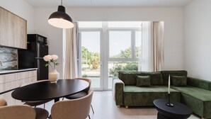 A modern living room with a green sofa, a dining table with chairs, a black pendant light, and a kitchen area with a microwave. - Comfort and Design Facing the Turia Gardens in Valencia (Valencia)