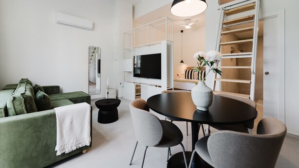 A modern living room with a green sofa, a round dining table, and a TV mounted on a white wall. - Comfort and Design Facing the Turia Gardens in Valencia (Valencia)