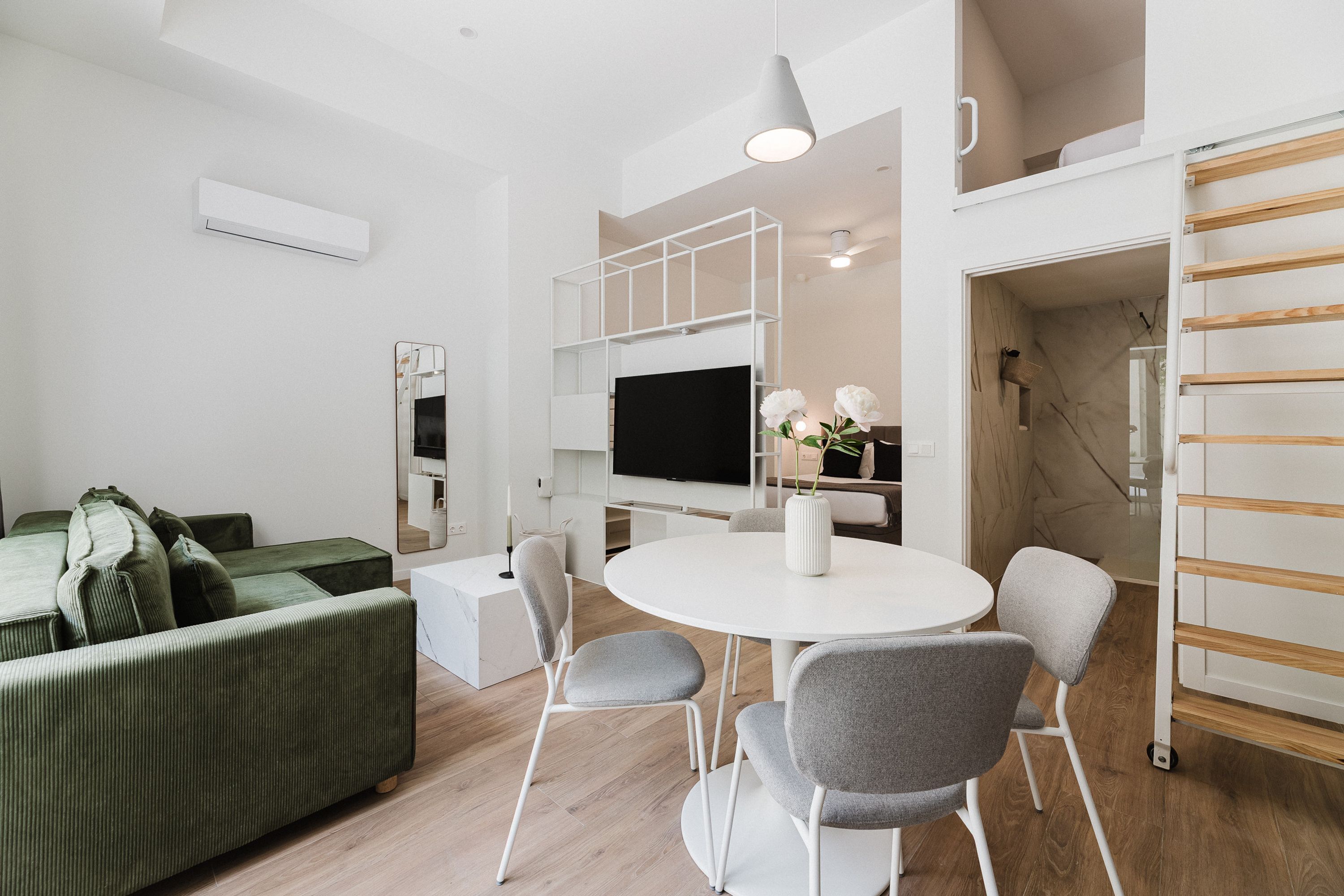 A modern living room with a green sofa, white round table, and grey chairs.