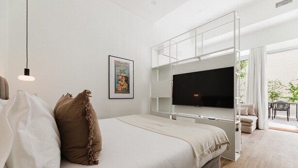 A modern bedroom with a bed, a flat-screen TV, a framed picture, and a balcony with outdoor furniture. - Comfort Design and a Terrace Facing the Turia Gardens in Valencia (Valencia)