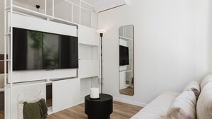 A modern living room with a flat-screen TV, a standing lamp, a round black side table, a white sofa, and a large mirror on the wall. - Comfort Design and a Terrace Facing the Turia Gardens in Valencia (Valencia)