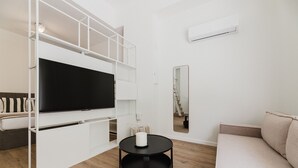 Uma sala de estar moderna com uma TV de tela plana, uma mesa de centro redonda preta, um sofá bege e uma estante branca.