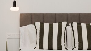 Uma cama com almofadas listradas, cabeceira cinzenta e mesa de cabeceira com abajur.