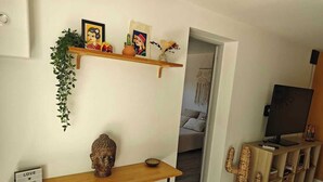 Een woonkamer met een houten consoles, een cactussculptuur, een televisie op een standaard en een doorgang naar een andere kamer.