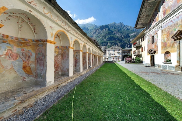A courtyard with a green lawn, a cobblestone path, and buildings with frescoed walls.