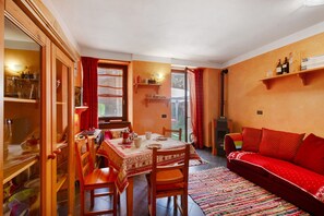 A dining area with a table set for four, wooden chairs, and a red sofa in a room with orange walls and a window.