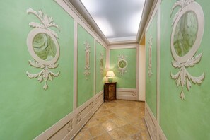 A hallway with green walls, ornate mirrors, and a tiled floor.