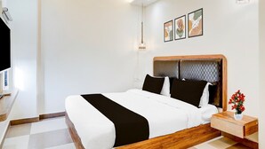A modern hotel room with a large bed, a wooden headboard, a bedside table with a vase of flowers, and a wall-mounted TV. - Deluxe Collection O Mahabalipuram (Tirukalukundram)